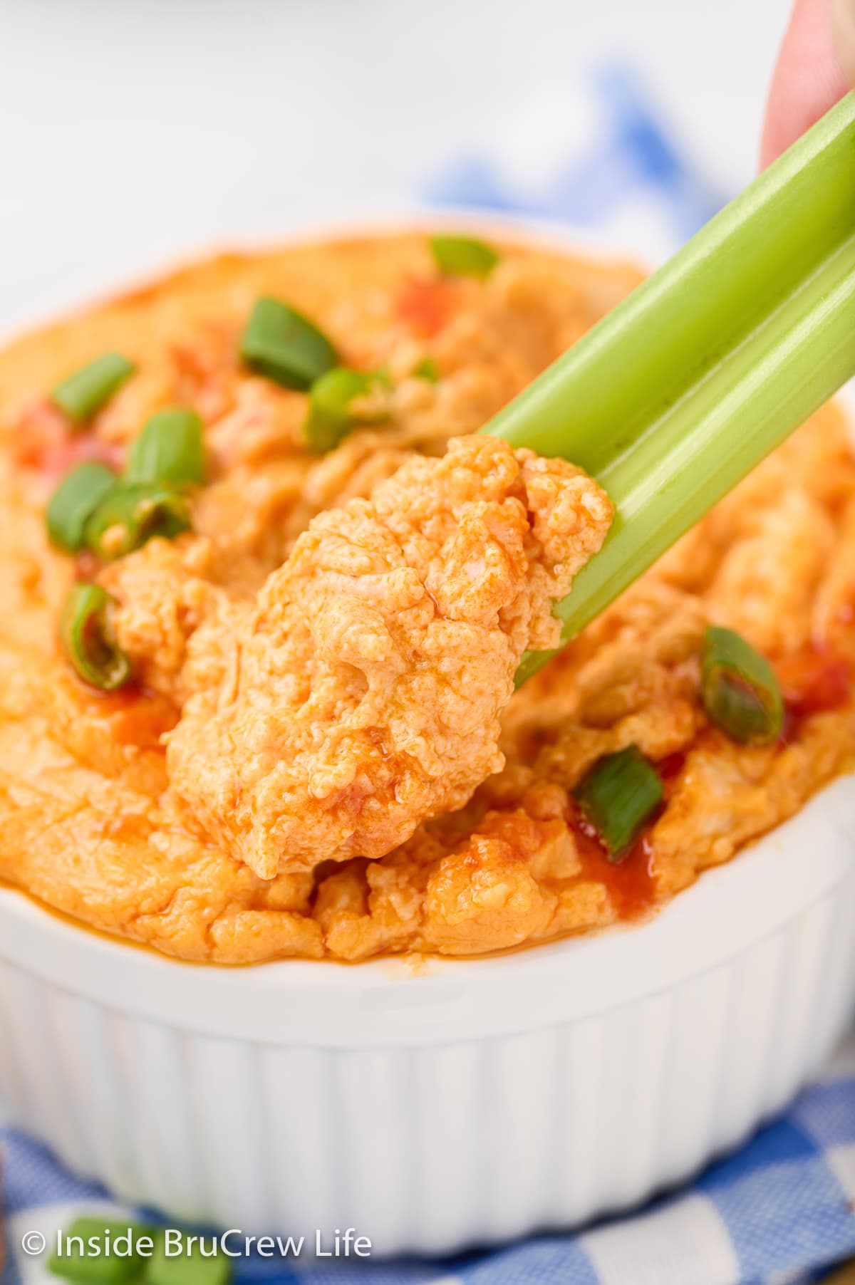 A white bowl with a stalk of celery dipping into a cheesy dip.