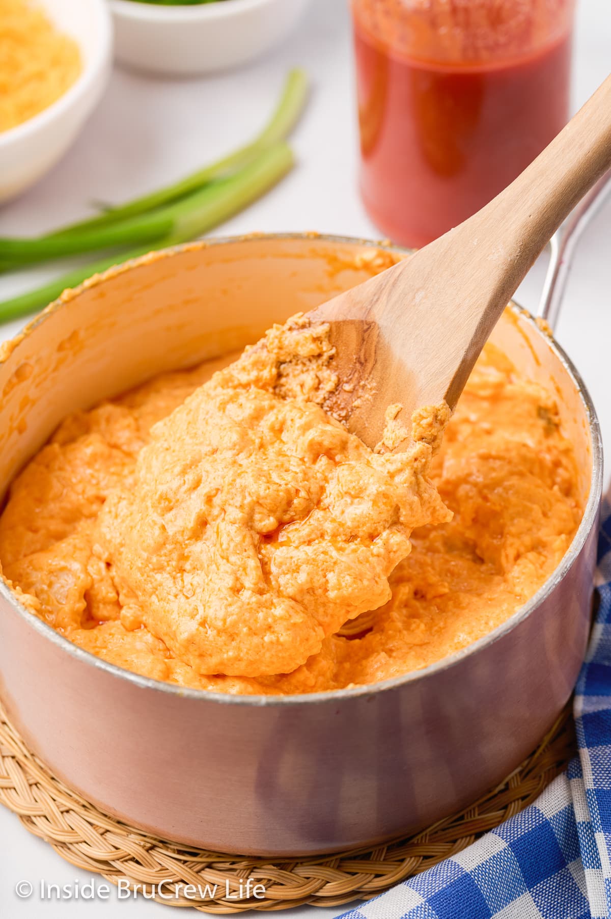 A pan of cheesy chicken dip with a wooden spoon stirring it.