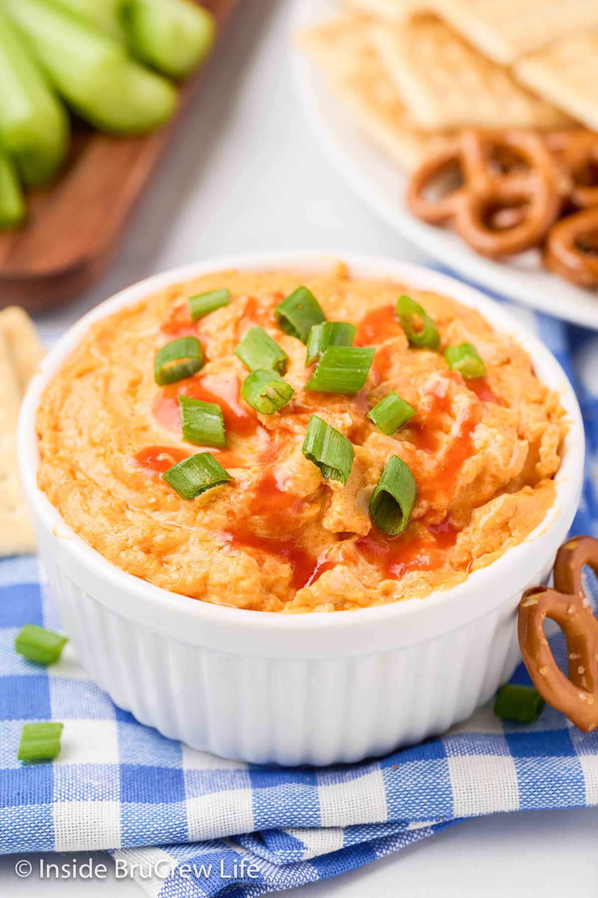 A white bowl filled with cheesy dip topped with hot sauce and green onions.