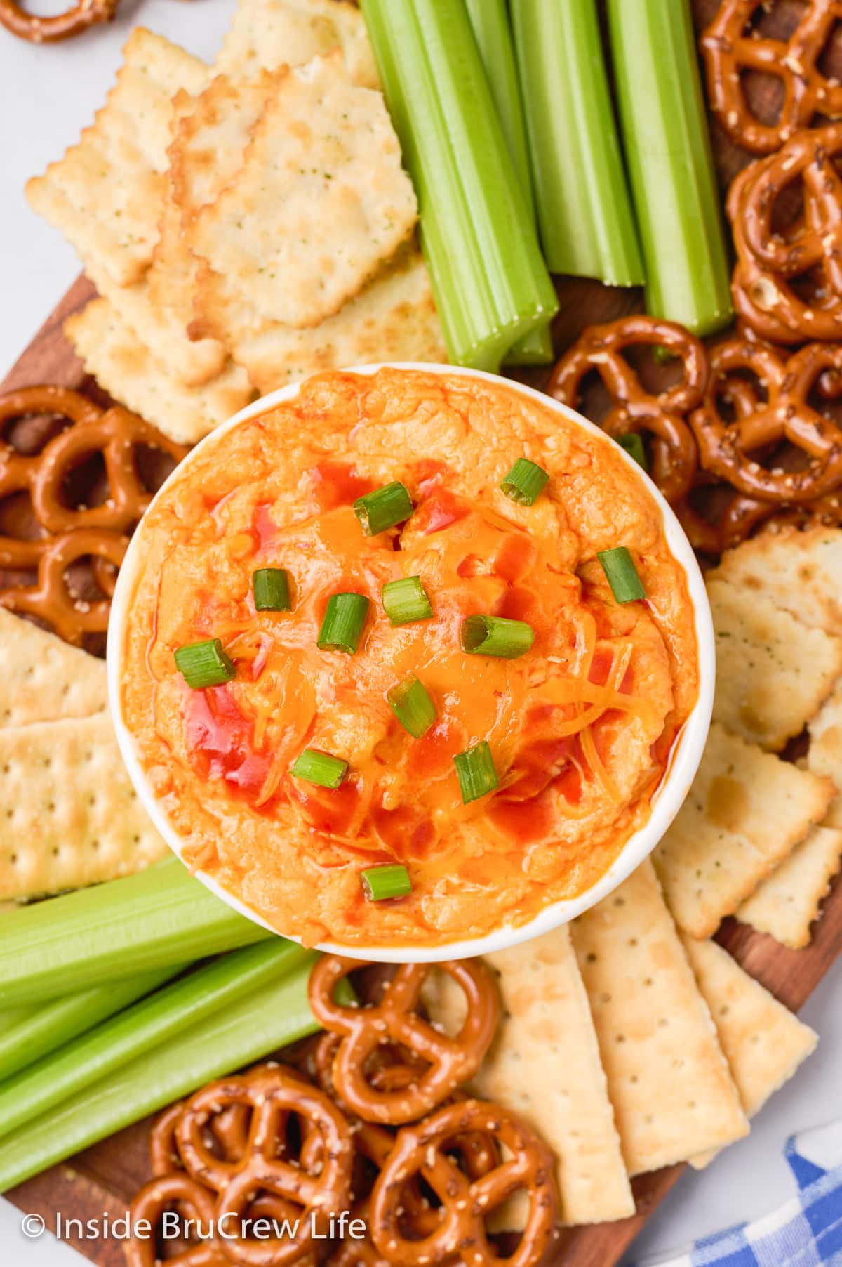 A cheesy dip bowl on a tray with pretzels, crackers, and celery.