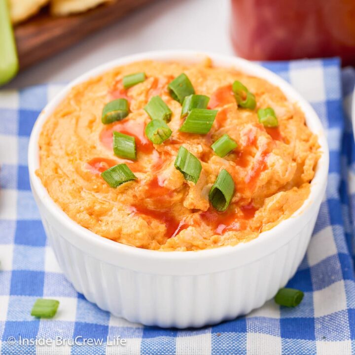 A white bowl filled with cheesy dip topped with hot sauce and green onions.