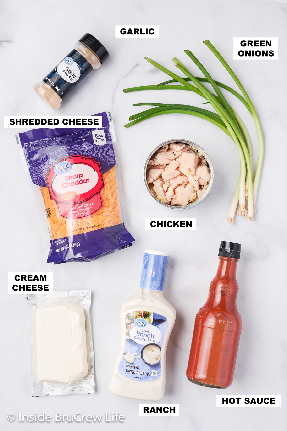 A white board with bowls and bottles of ingredients needed to make a spicy chicken dip.