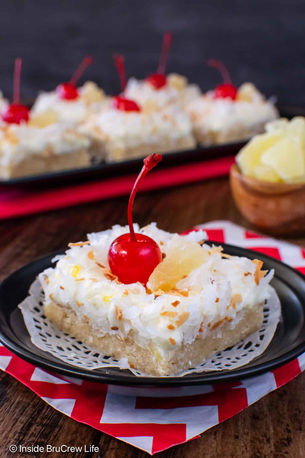 A pina colada bar topped with coconut and a cherry on a black plate.