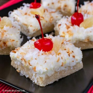 Squares of pina colada cookie bars with coconut on a black plate.