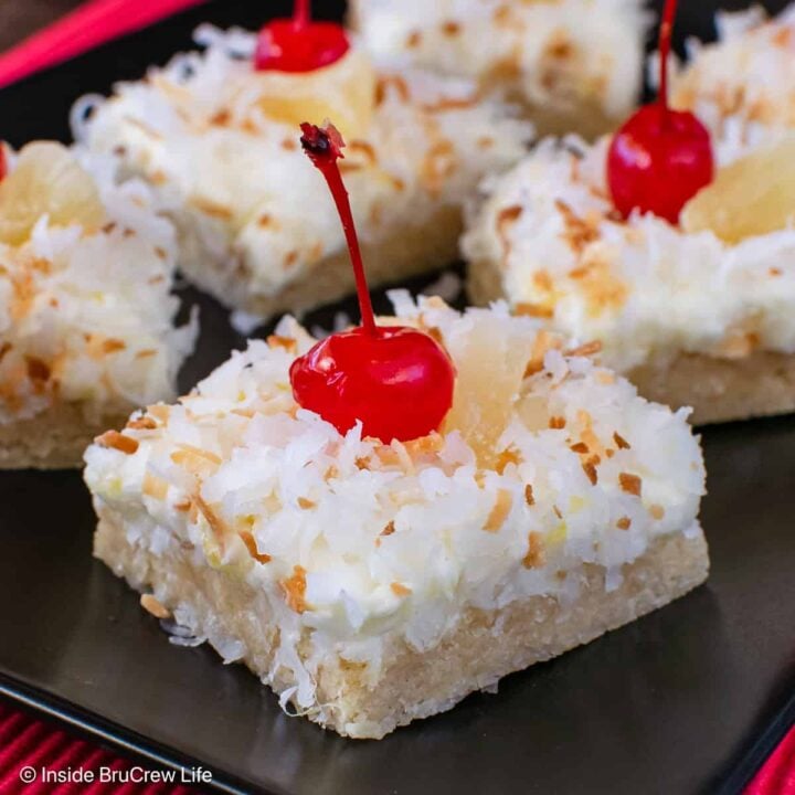 Squares of pina colada cookie bars with coconut on a black plate.