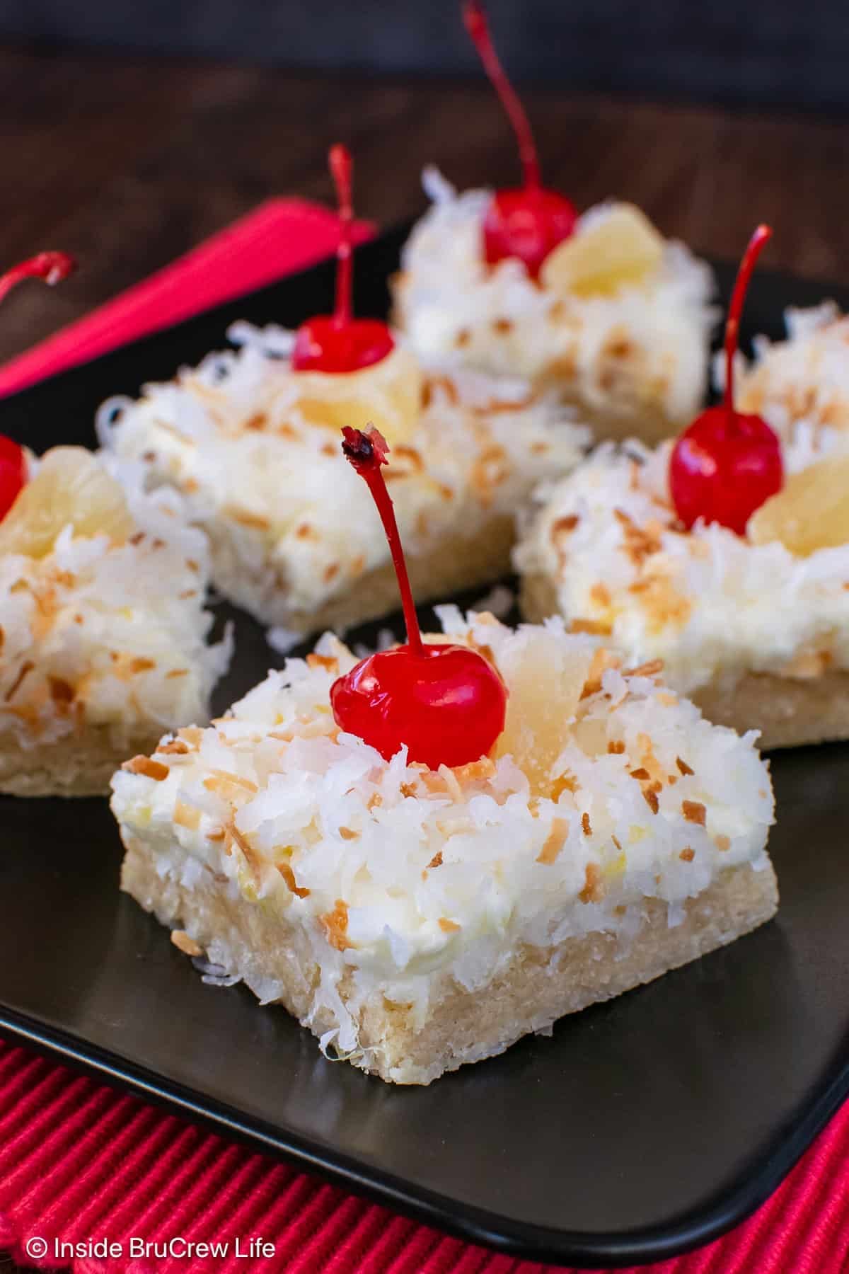 Squares of pina colada cookie bars with coconut on a black plate.