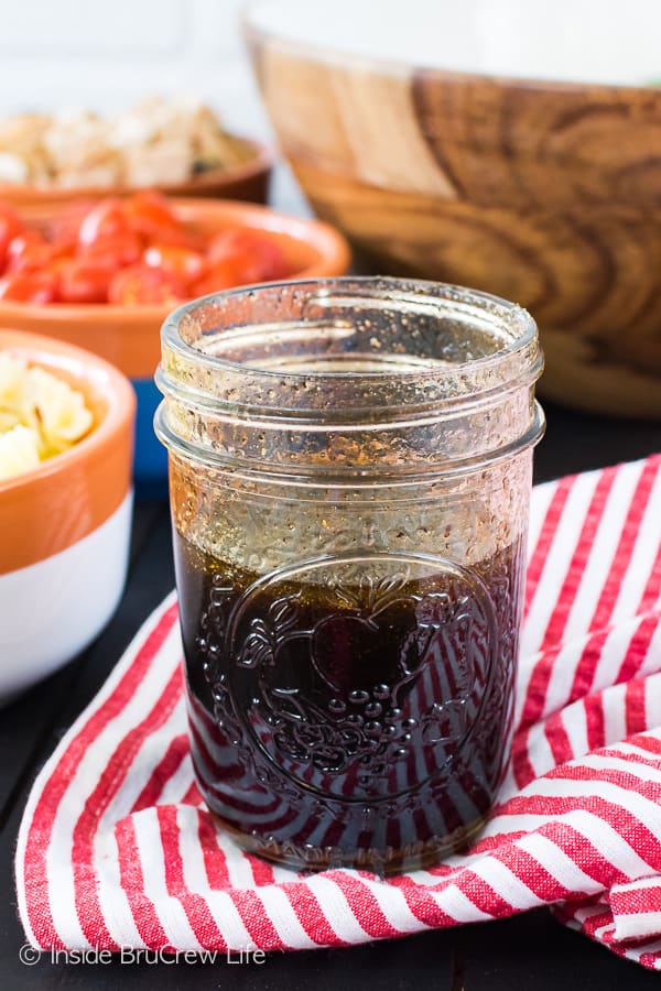 A jar of balsamic vinaigrette sitting on a red and white striped towel with a bowl of salad behind it