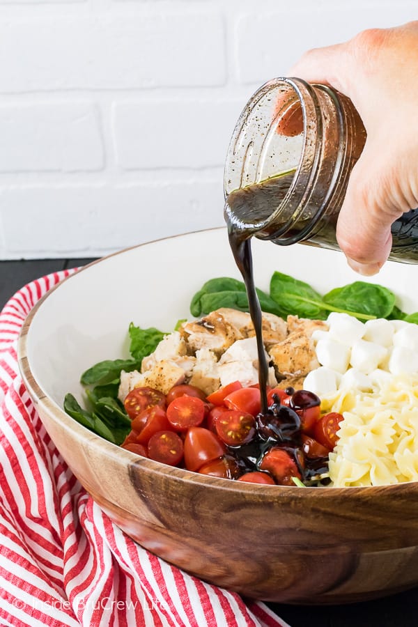 A jar of balsamic vinaigrette being poured into a big bowl of salad