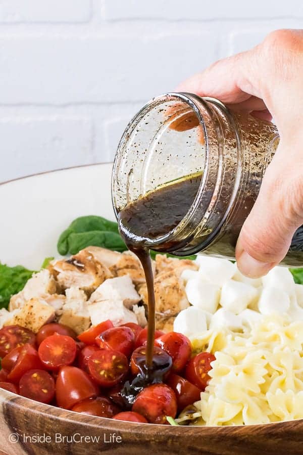 Ein Glas Balsamico-Vinaigrette wird über einen Hähnchen-Caprese-Salat gegossen