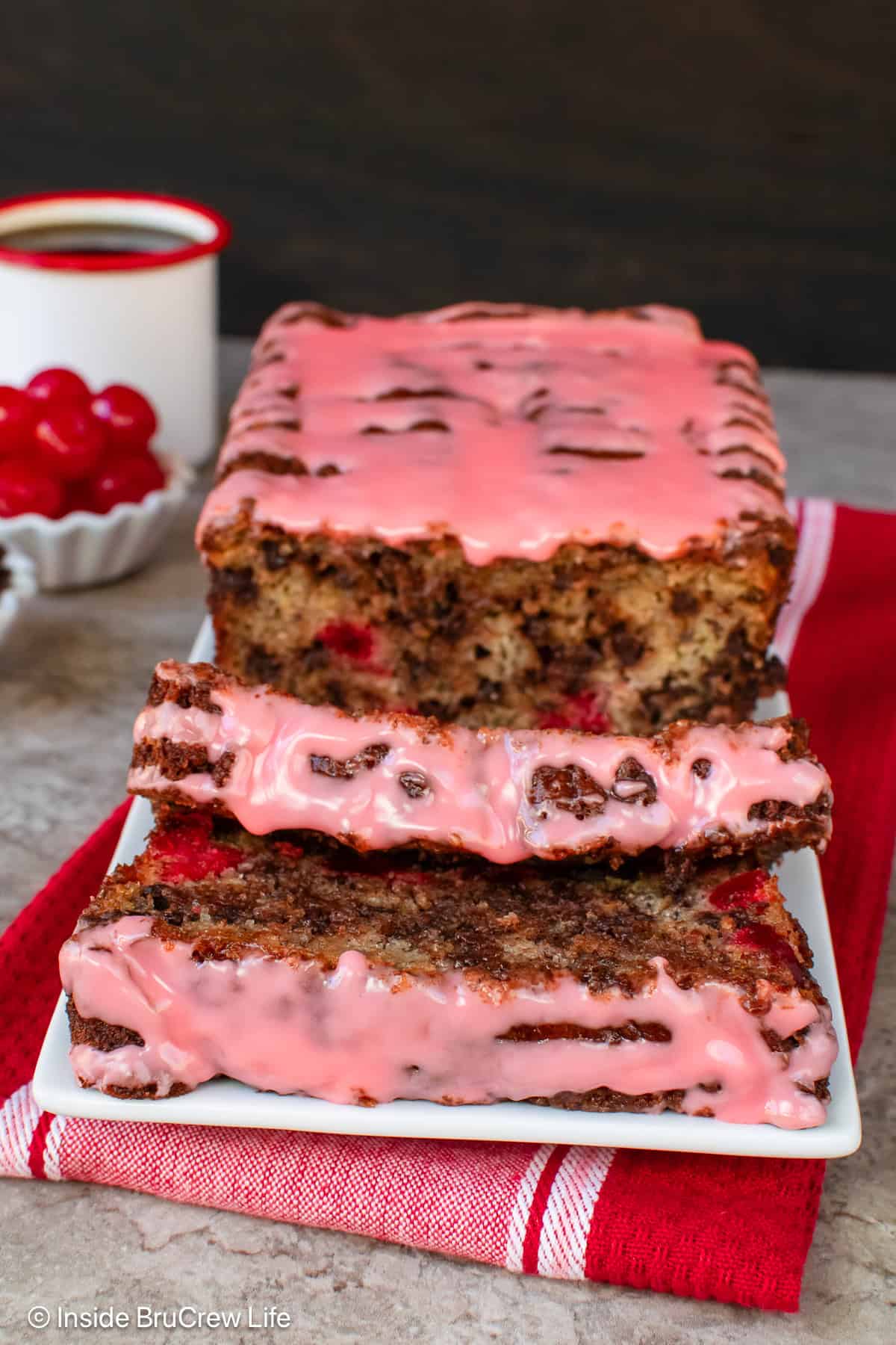 A loaf of cherry banana bread with pink glaze sliced and on a white plate.
