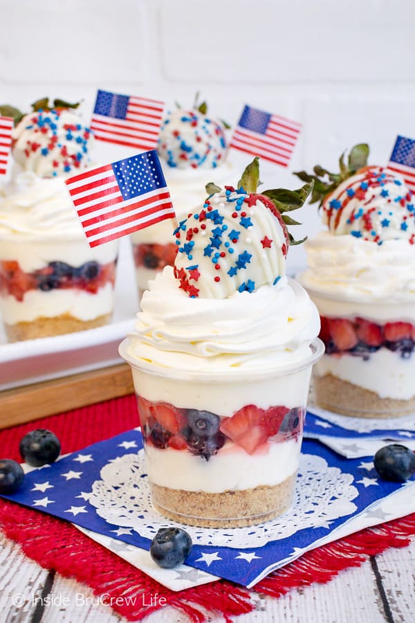 Clear cups filled with cheesecake mousse, fruit, and cool whip on blue and red napkins.