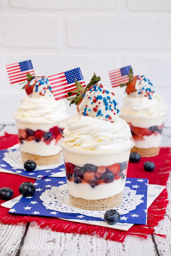 Three cheesecake parfaits with layers of white chocolate mousse and fresh fruit on red white and blue napkins.