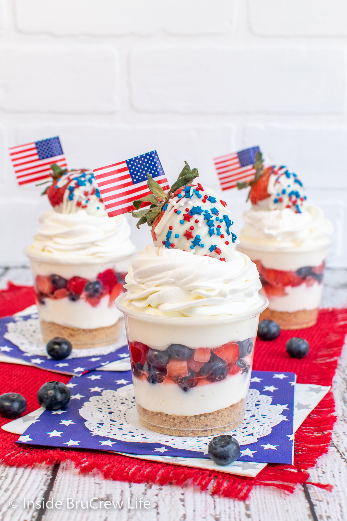 Three cheesecake cups with layers of blueberries and strawberries in the middle.