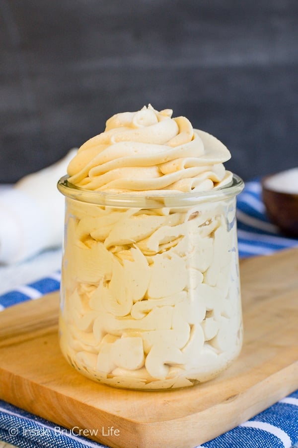 A clear jar filled with a swirl of salted caramel frosting on a brown board.