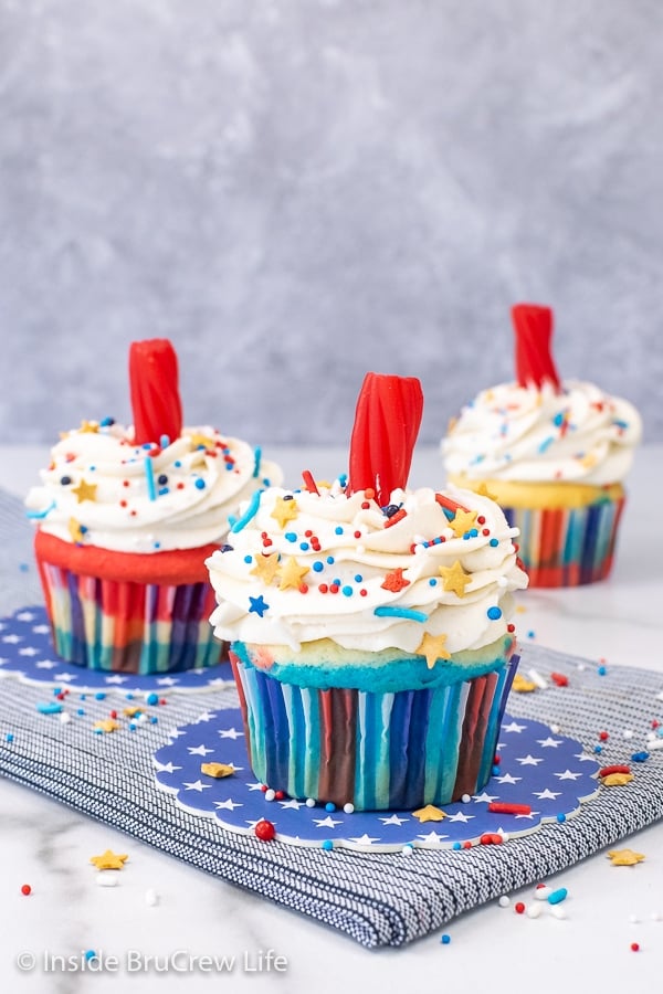 Three firecracker cupcakes decorated with vanilla frosting, sprinkles, and a Twizzler "fuse".