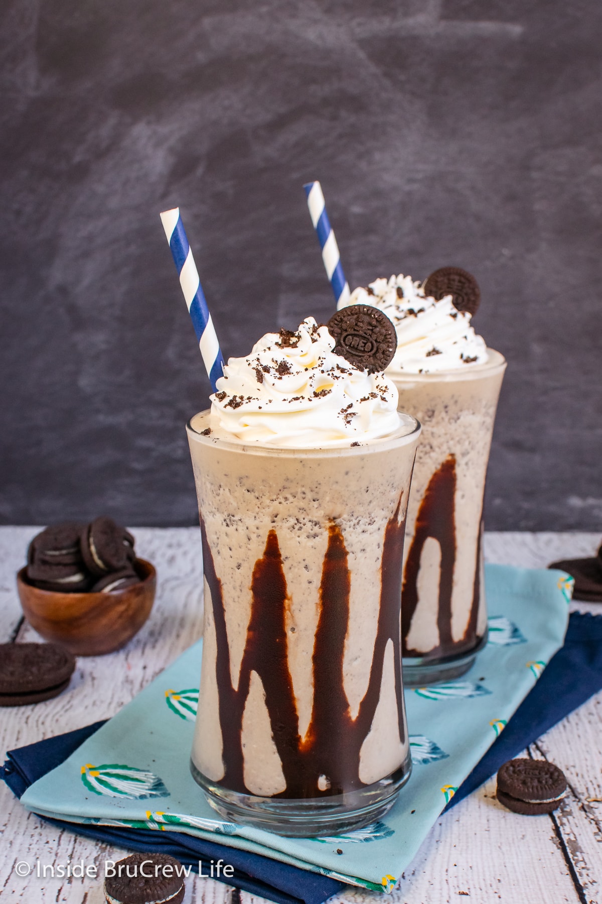 Two clear cups drizzled with chocolate and filled with a cookie shake.