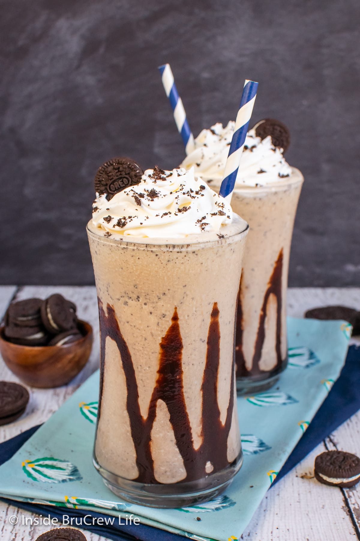 Two cups filled with an Oreo shake and drizzled with chocolate syrup.