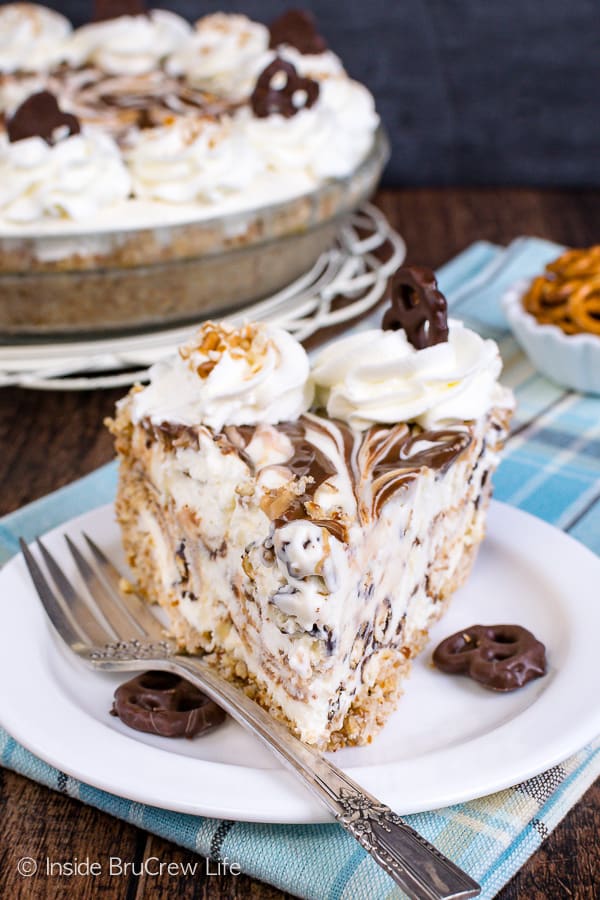 A slice of ice cream pie on a white plate with a fork and the rest of the pie behind it.