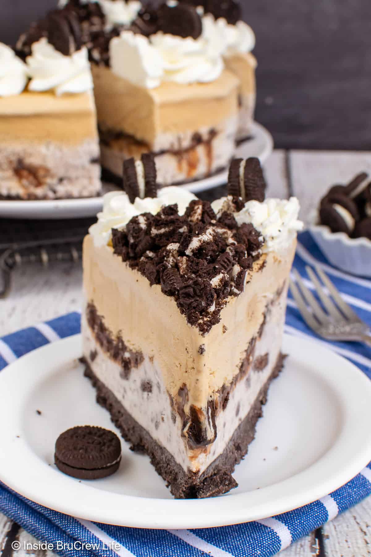 A slice of Oreo coffee ice cream cake on a plate with the cake behind it.