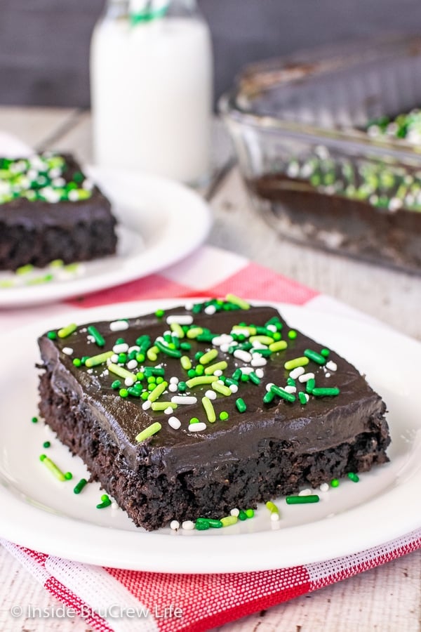 A white plate with a square of chocolate zucchini cake topped with dark chocolate frosting and sprinkles.