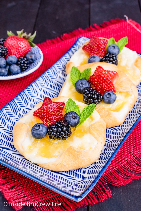 A white and blue plate with three lemon cheese danishes topped with fruit on it.