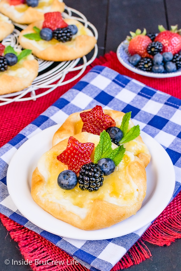 A white plate with a cheese danish topped with lemon curd and fresh fruit on it.