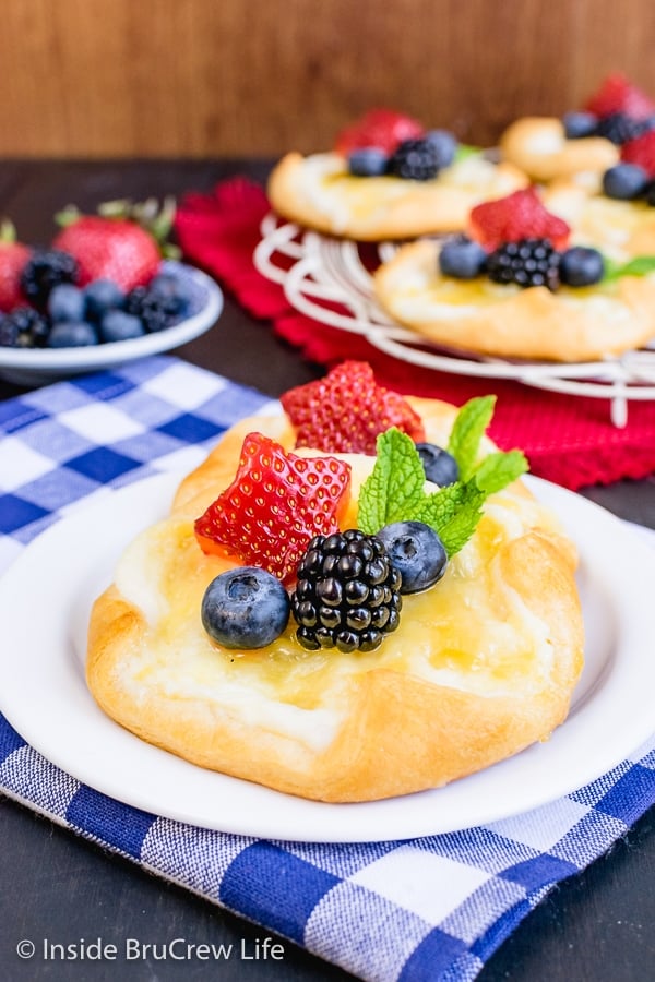 A white plate with two cheese danishes topped with lemon curd and fresh berries on it.