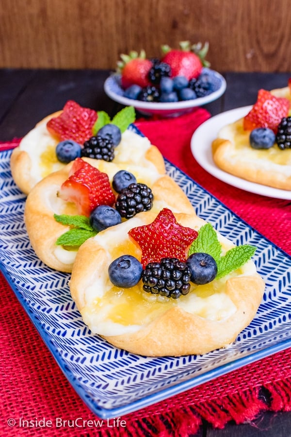 A blue and white plate with three cream cheese danishes topped with lemon curd and fresh fruit on it.