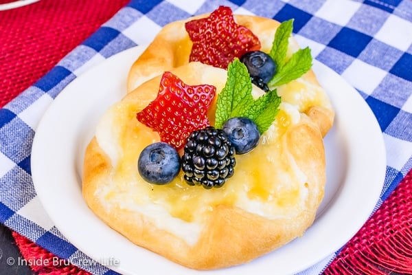 Two lemon cheese danishes topped with fresh berries and mint leaves on a white plate.