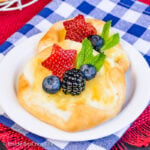 A white plate with two lemon cheese danishes topped with fresh berries.