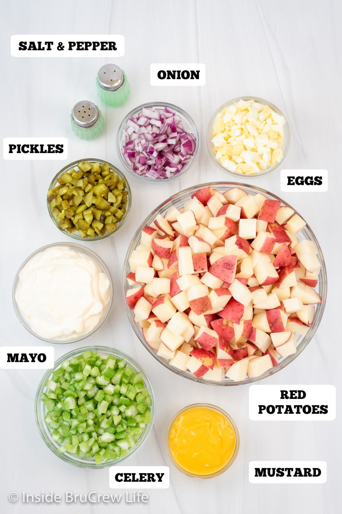 A white board with bowls of ingredients needed to make potato salad.