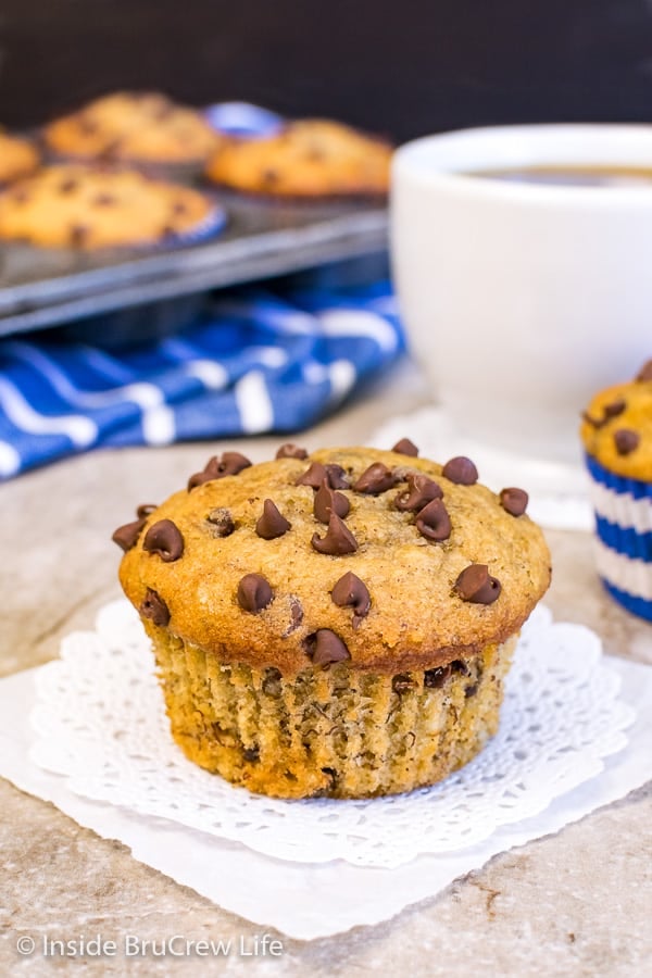 A white doily with a peanut butter chocolate chip banana muffin on it and a muffin tin behind it.