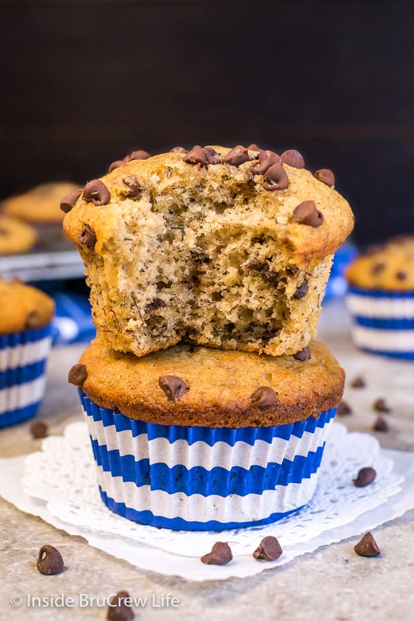 Two peanut butter banana muffins in blue and white liners stacked on top of each other with a bite out of the top muffin.