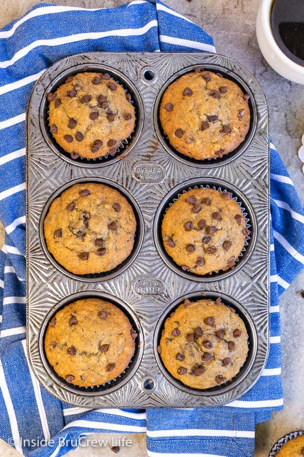 Overhead picture of 6 peanut butter chocolate chip banana muffins in a muffin tin on a blue towel.