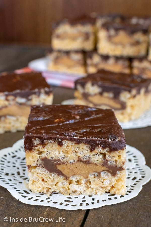 Squares of peanut butter rice krispie treats with a layer of peanut butter cups in them on a brown board