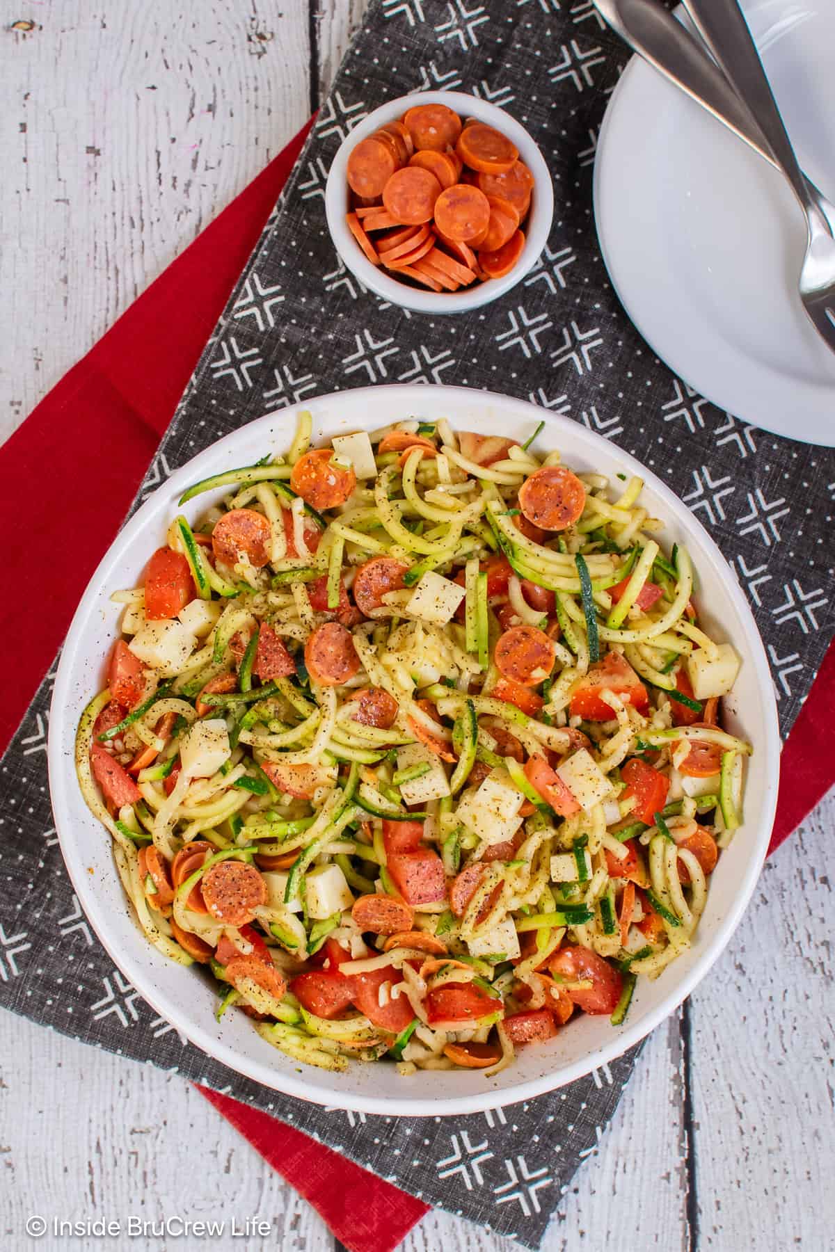 An overhead picture of a large bowl of zucchini noodle salad with pizza toppings.