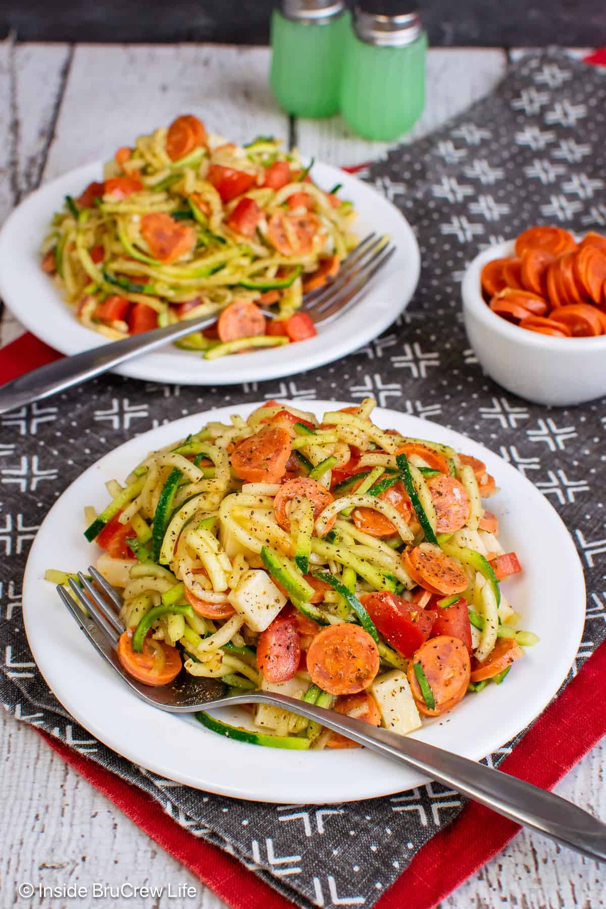 Two white plates with pizza zucchini noodle salad on it.