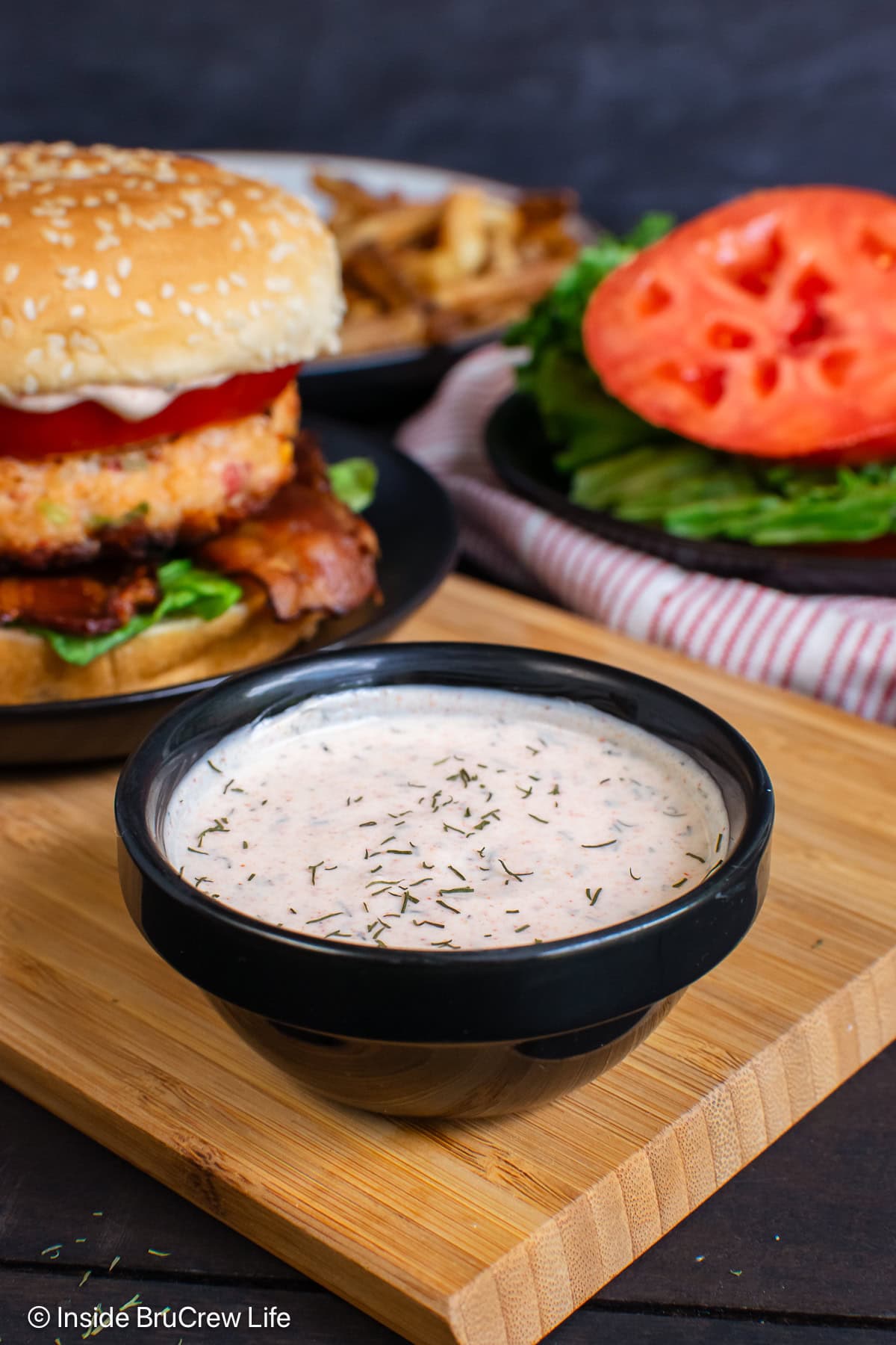 A bowl of dill mayo beside a shrimp burger.