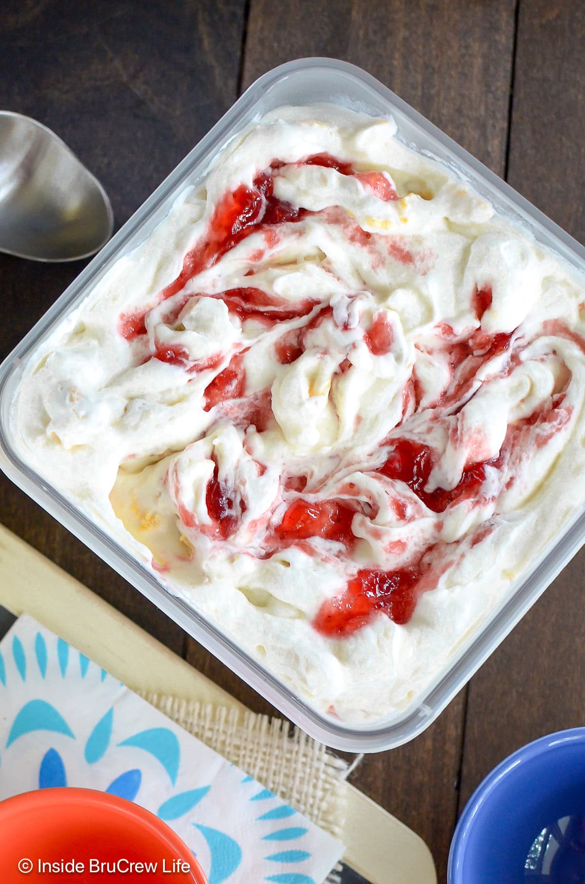 A container of frozen no churn lemon ice cream with strawberry swirls.