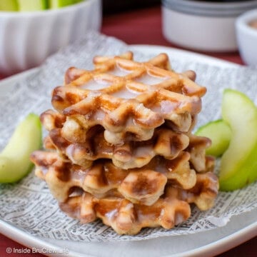 A stack of waffle donuts on a plate with apple slices.