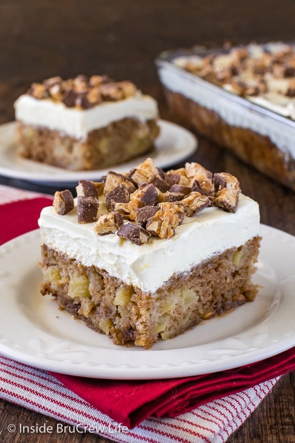 A close up picture of a piece of apple Snickers cake topped with chopped up Snickers candy bars