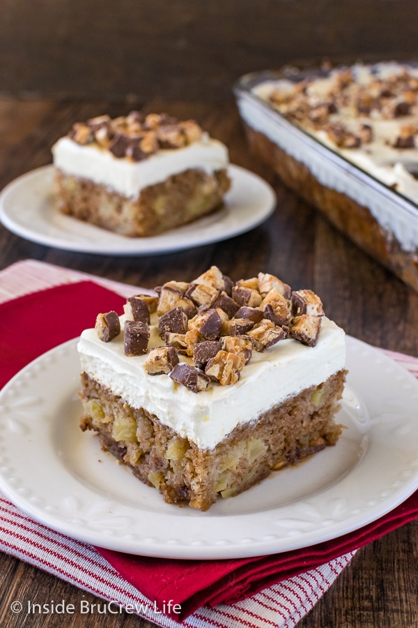 Two squares of apple Snickers cake on white plates with a pan of cake beside them