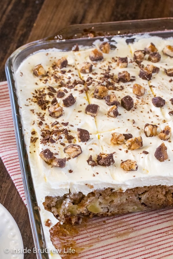An overhead picture of a pan of apple cake topped with a fluffy frosting and Snickers bars