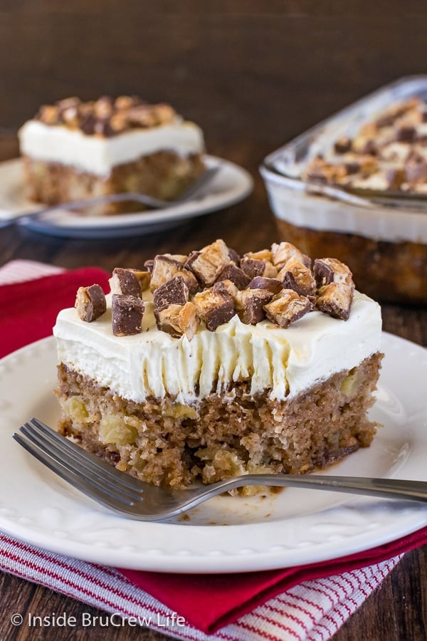 A piece of apple Snickers cake with fluffy frosting on a white plate with a bite take out of it