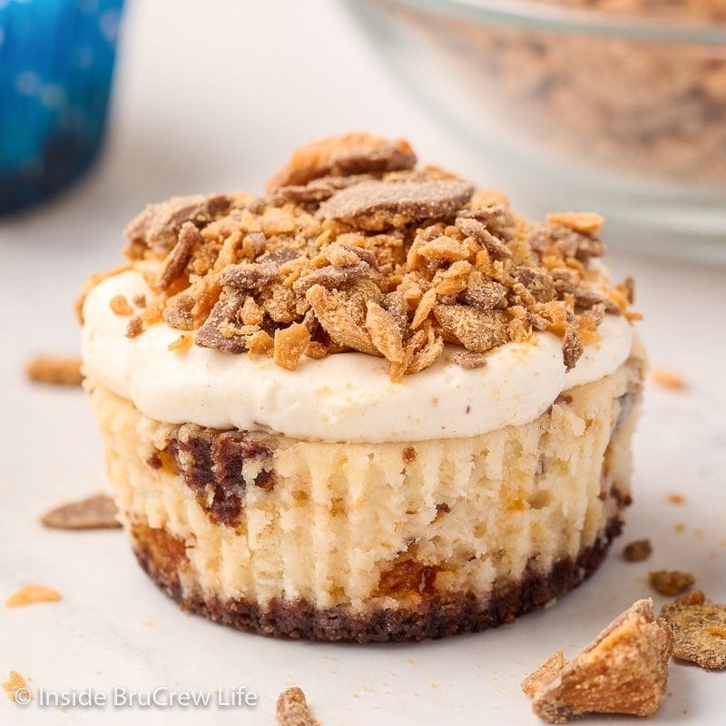 A cheesecake cupcake with Butterfinger pieces on top.