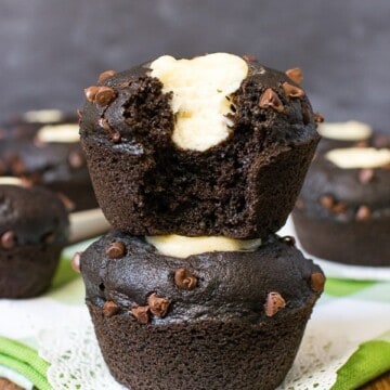 Two chocolate zucchini cheesecake muffins stacked on top of each other with a bite out of the top one