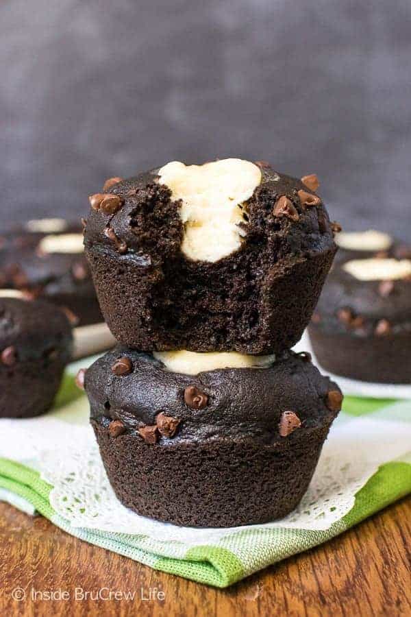 Two chocolate zucchini cream cheese muffins stacked on top of each other with a bite out of the top one