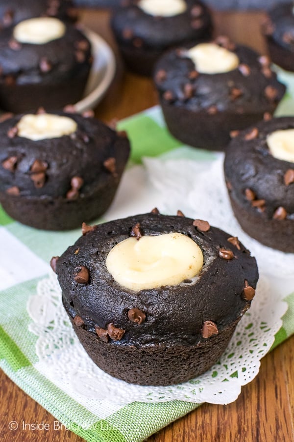 Chocolate Zucchini Cream Cheese Muffins with chocolate chips on a wood board with a green and white towel