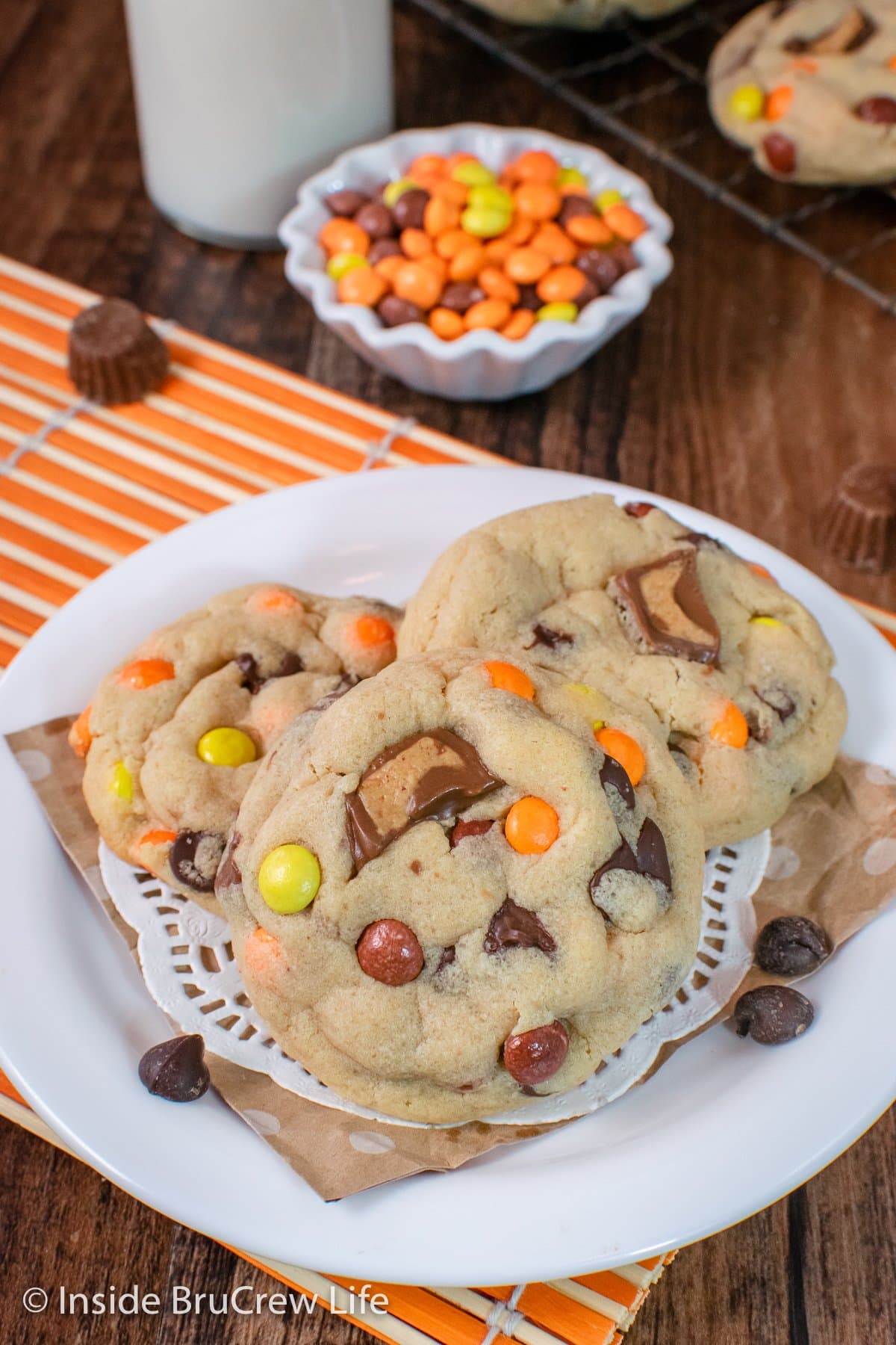 Three peanut butter cookies with Reese's candies in them on a white plate.