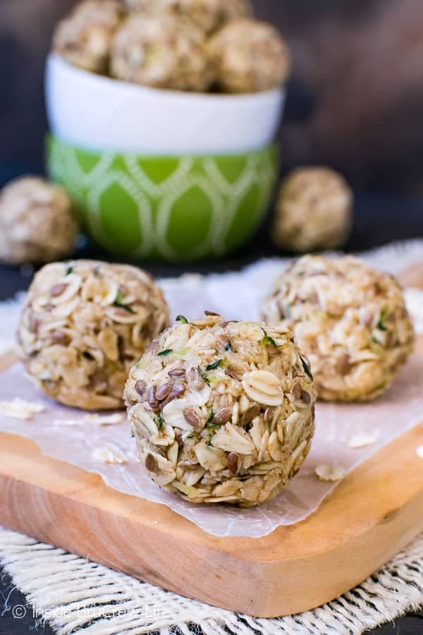 Three zucchini oatmeal bites on a wood tray with a bowl of bites behind them